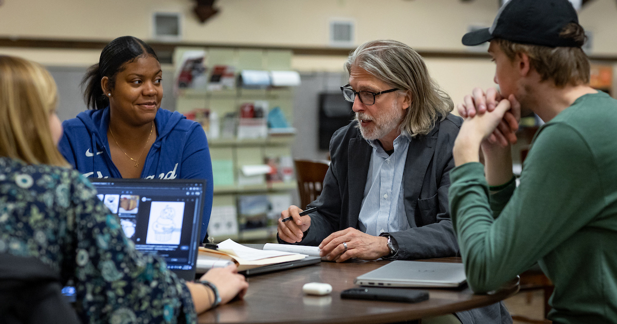 A man sits and talks with three students at a round table in the Ball State Learning Center
