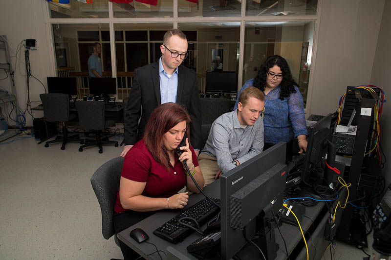 Four professionally-dressed people look at a computer monitor in a computer lab