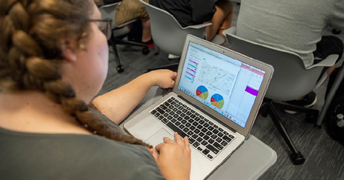 Ball State student works on their laptop in a classroom.