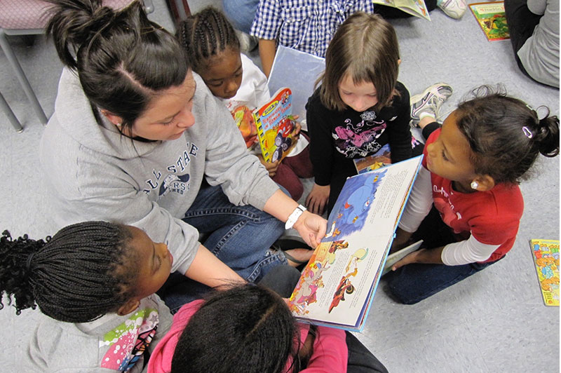 A student reading a book to a group of children.