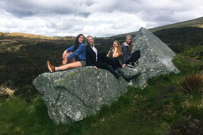 Student sitting on a rock and smiling.