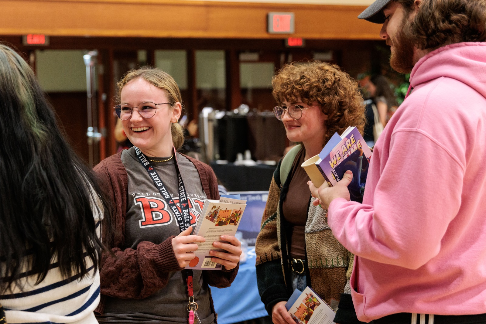 Three smiling Ball State University students chatting and holding informational brochures and books at a campus event