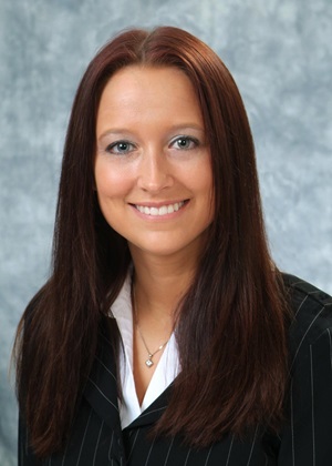 Headshot of a woman with reddish-brown hair smiling and wearing a black suit 