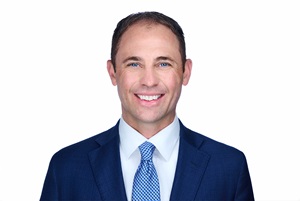 Headshot of Ryan Gard, smiling and wearing a suit with a blue tie and white undershirt.