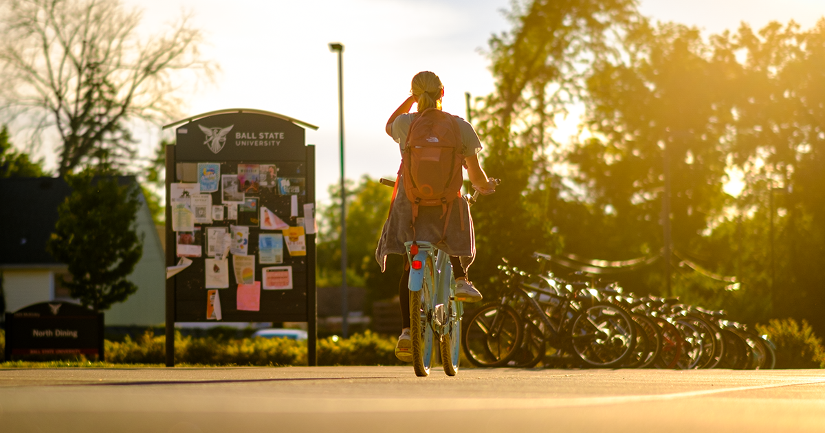 A student on campus biking with a backpack on during the sunset 