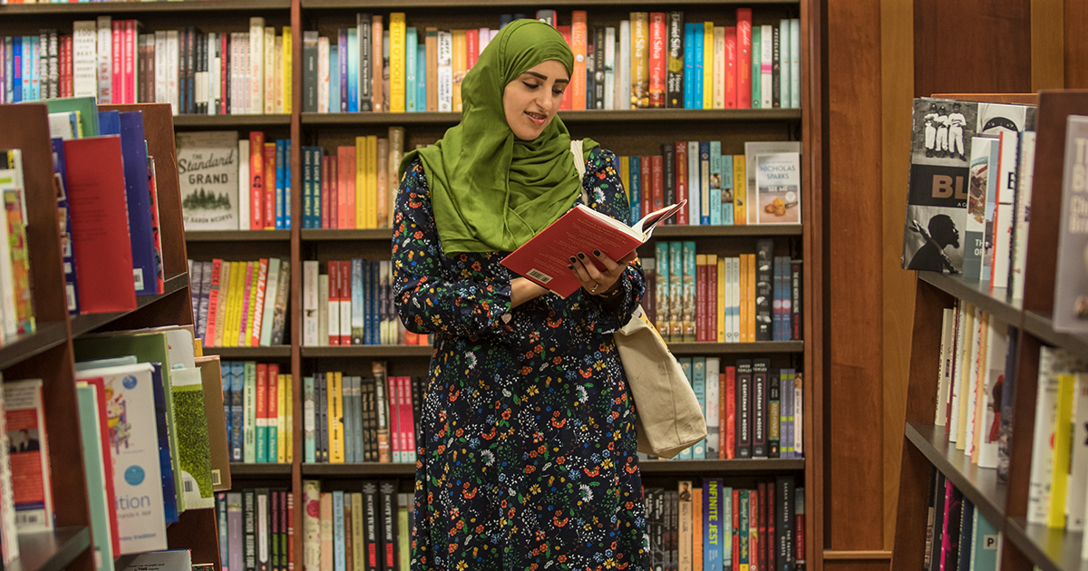 A Ball State student standing in front of a shelf of books reading 