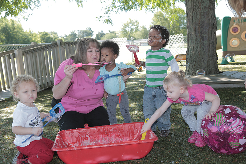 Toddlers blowing bubbles with teacher.