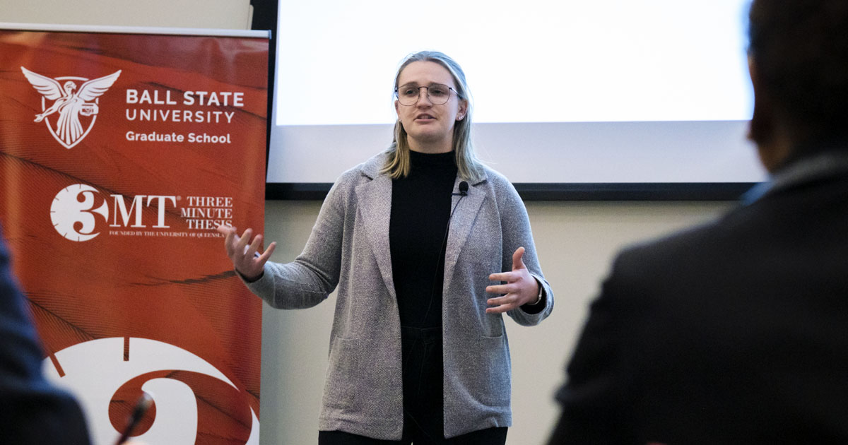 3 minute thesis presentation female presenter standing in front of projected screen