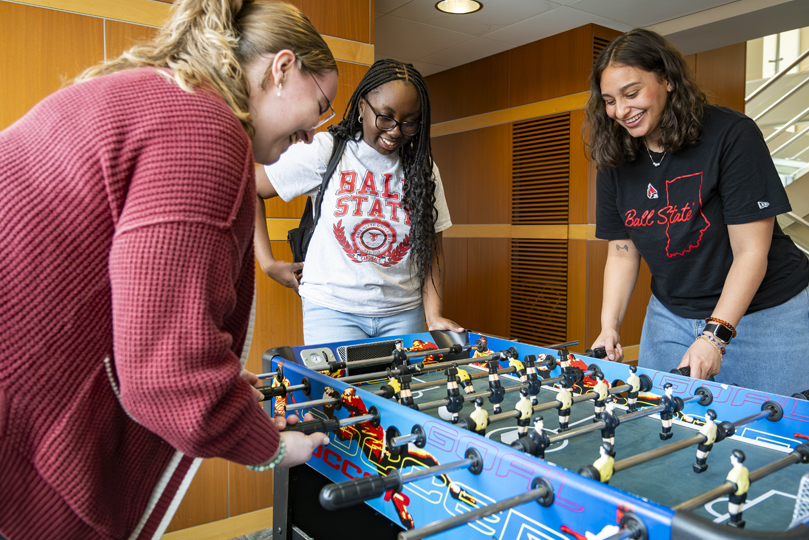 Three female students playing a game of foosball on a table in the lounge