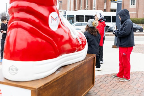 With a large red shoe in the foreground, students pass out flyers for the Walk-A-Mile event