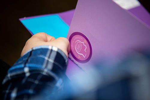 A hand holds a purple folder with the POP logo