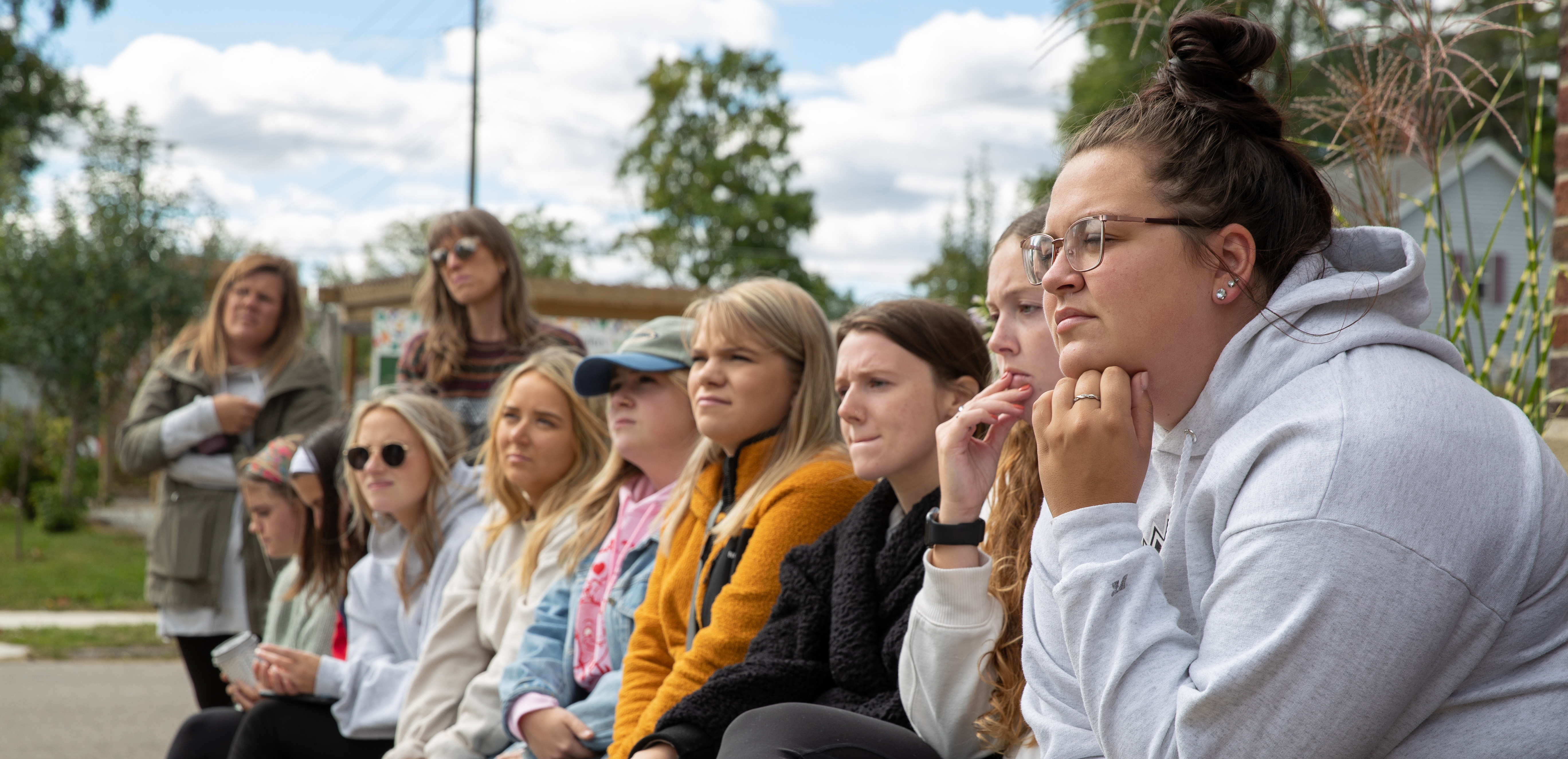 A group of students sit  outside listing to a speaker