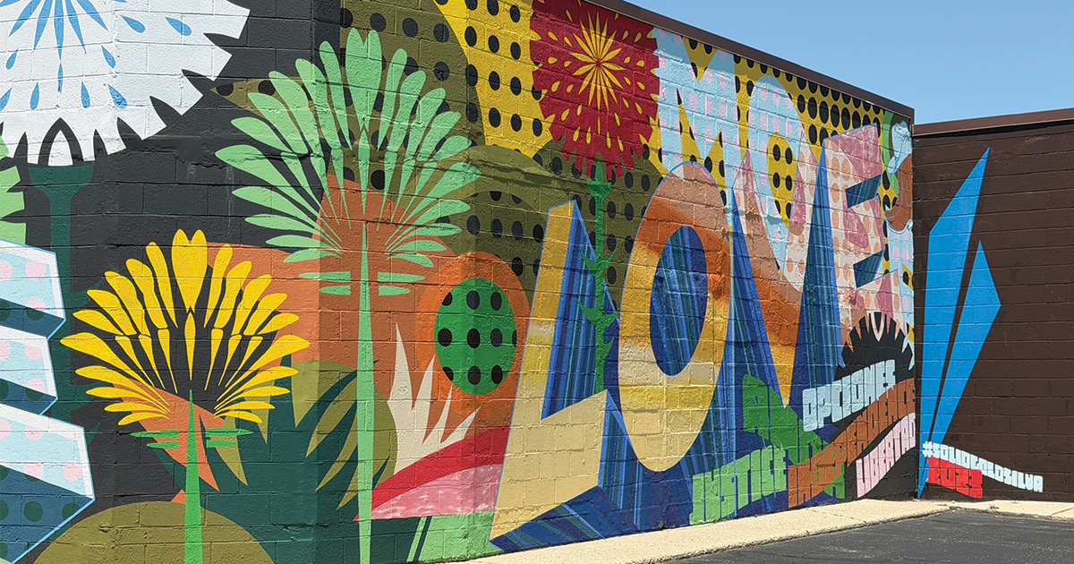 Colorful abstract mural painted on a brick wall, featuring oversized flowers, geometric shapes, and bold patterns.