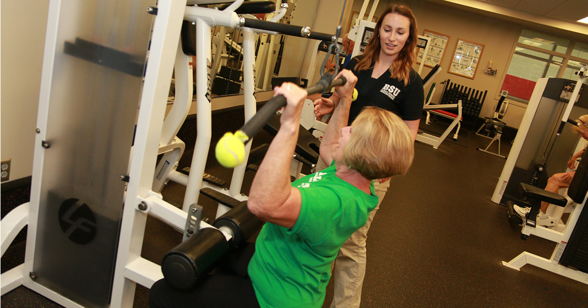 A woman lifts weights as a student supervises.
