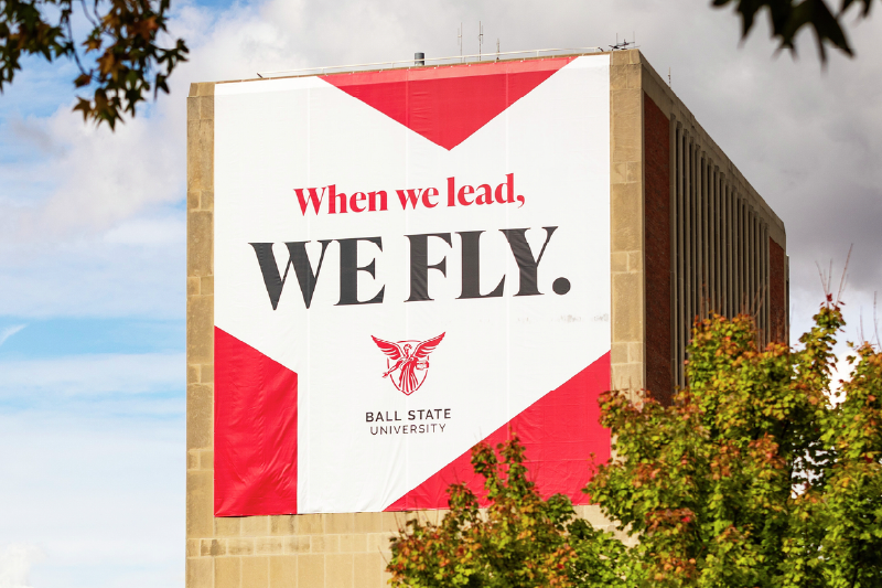 Sign on the side. of a building that reads,  "When we lead, we fly" with the Ball State logo.