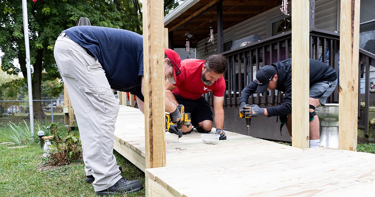 Volunteers build an accessibility ramp outside a home, using power tools during a community service project.