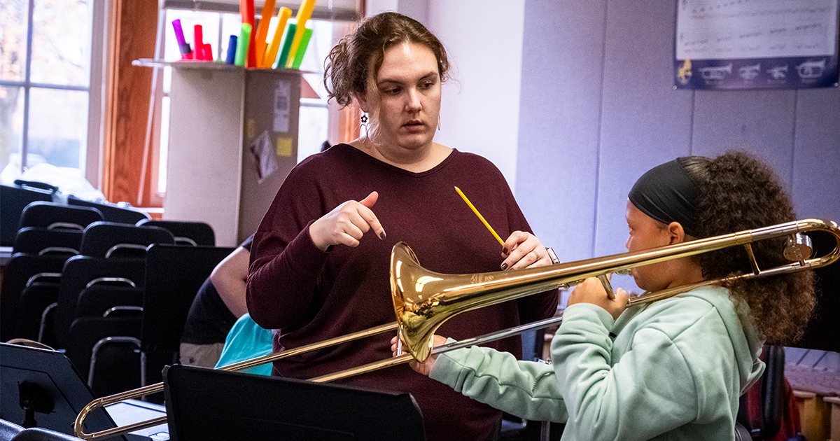 Ball State student teaching a young girl how to play a trumpet 