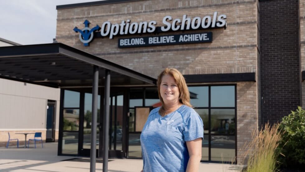 Karen Oliver looking at the camera while standing in front of a building with sign that says Options Schools