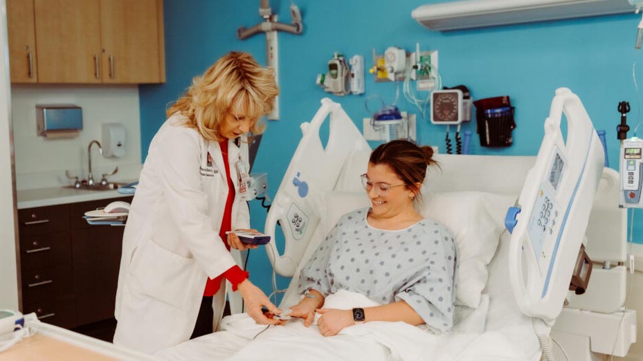 Renee Twibell stand's beside a patient's bedside, taking their pulse