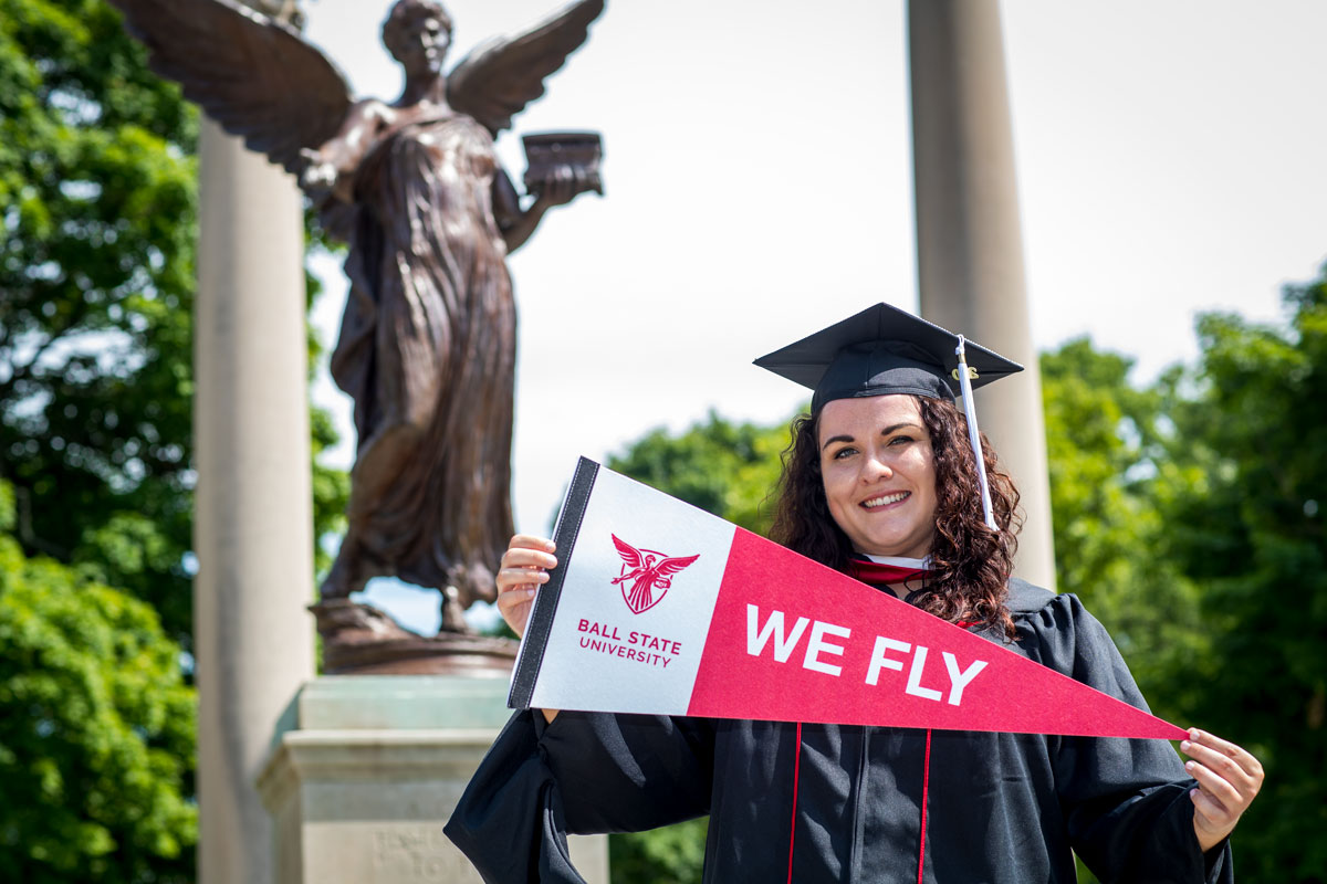Kaitlynn Holmes on campus, holding a Ball State pennant with "We Fly" slogan