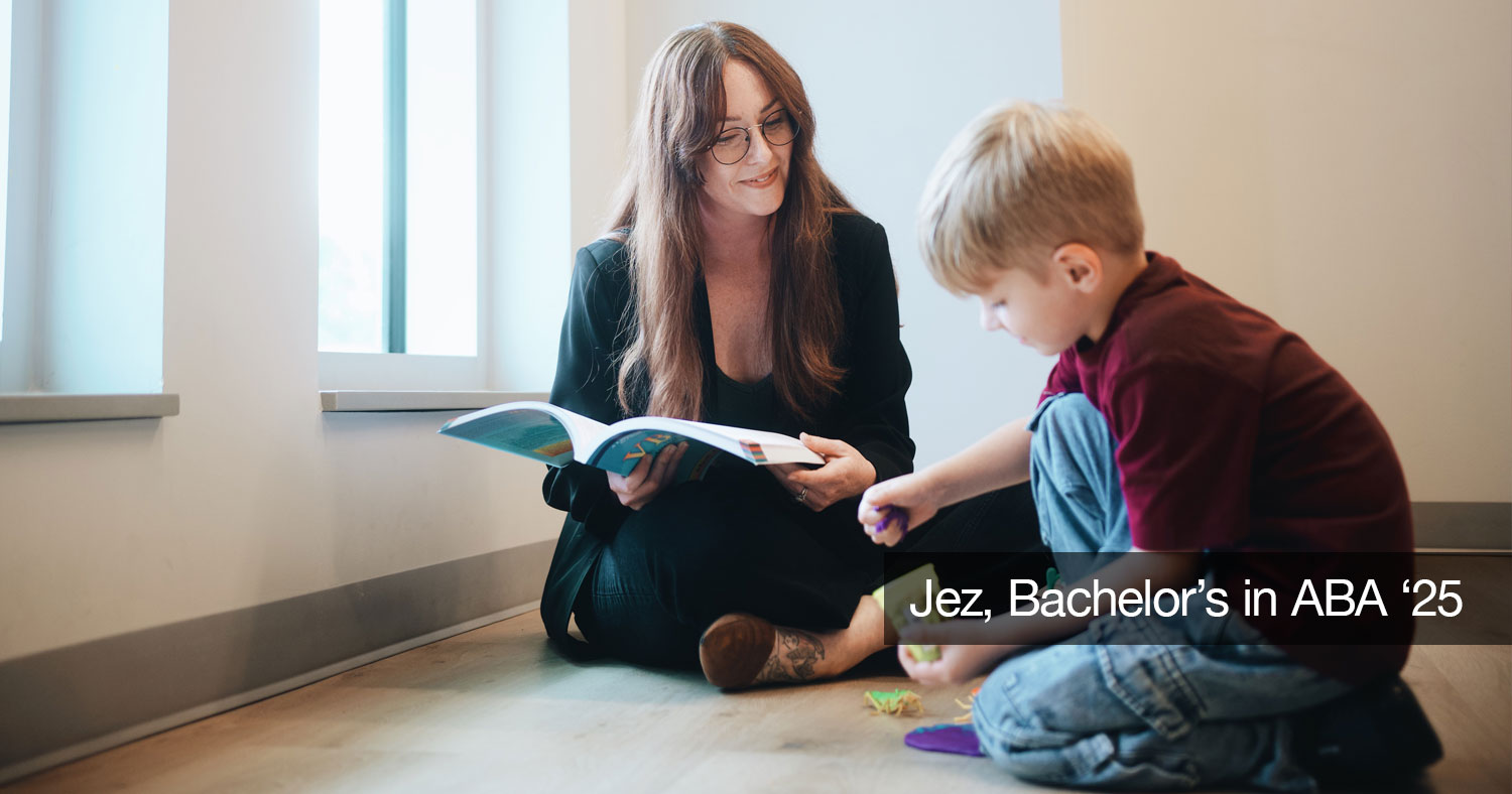 Jez Steffen reading a book while sitting on the ground next to a child