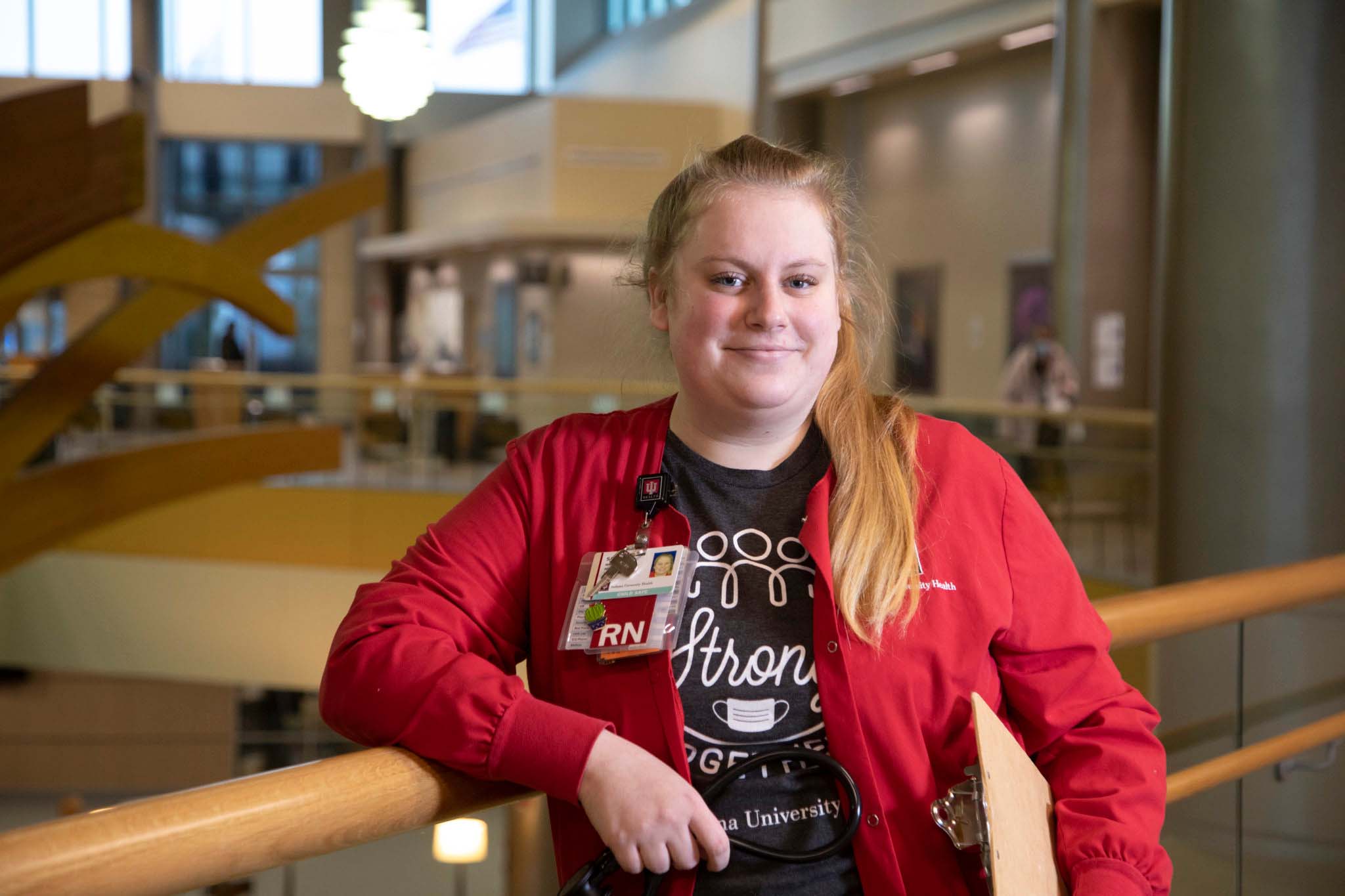 Female student nurse in red long sleeve shirt facing the camera smiling. 