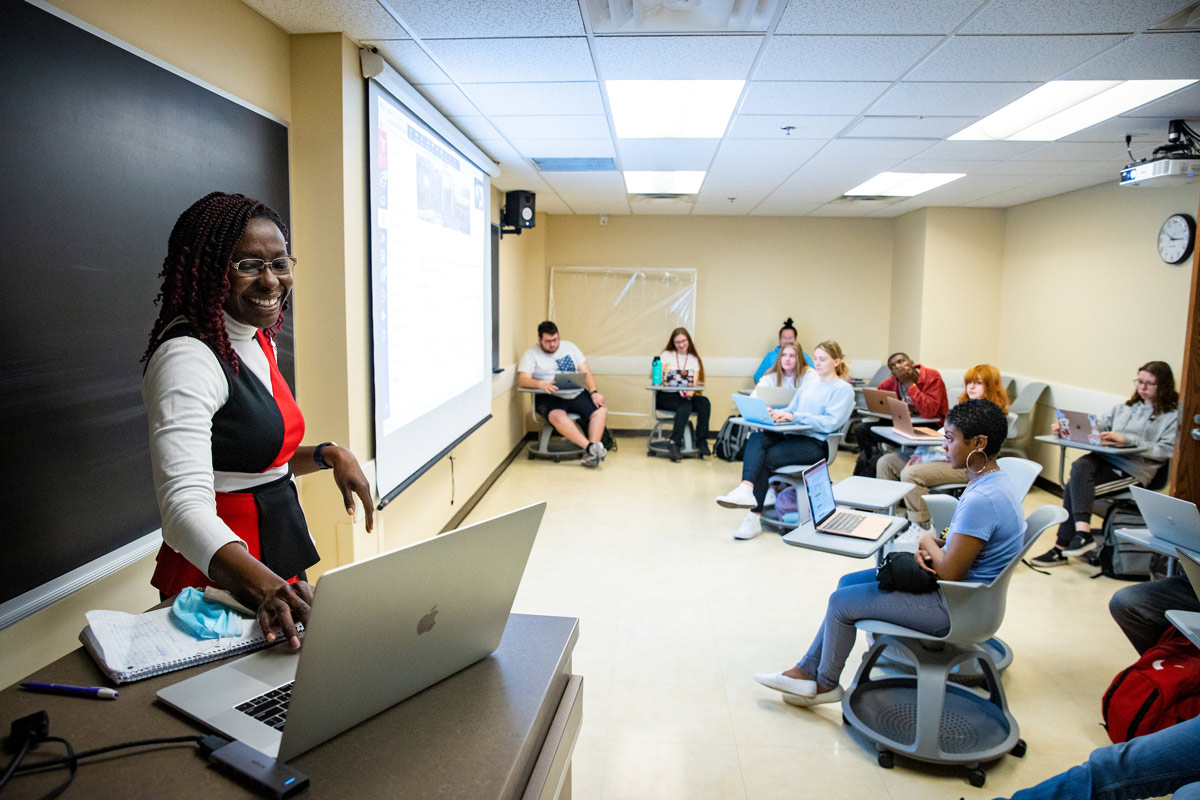 A faculty member uses a computer to share information with a class on a projection screen