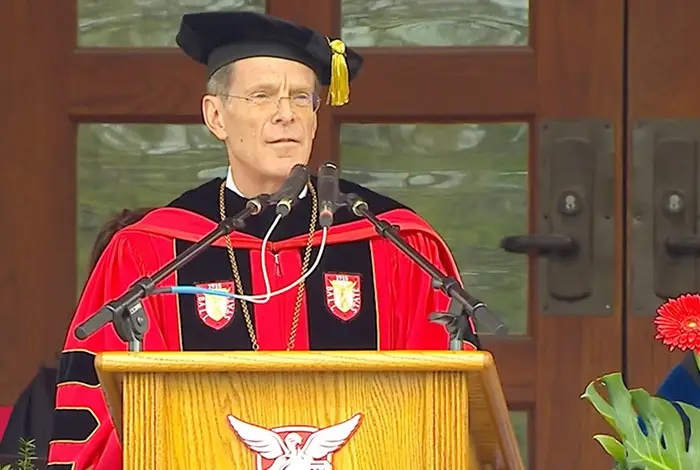 President Mearns speaks at a Ball State University event wearing academic regalia and addressing an audience from a podium 