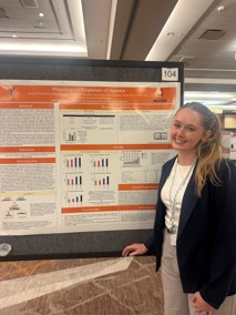 Avery Renshaw stands beside a research poster featuring charts and findings at an academic conference.