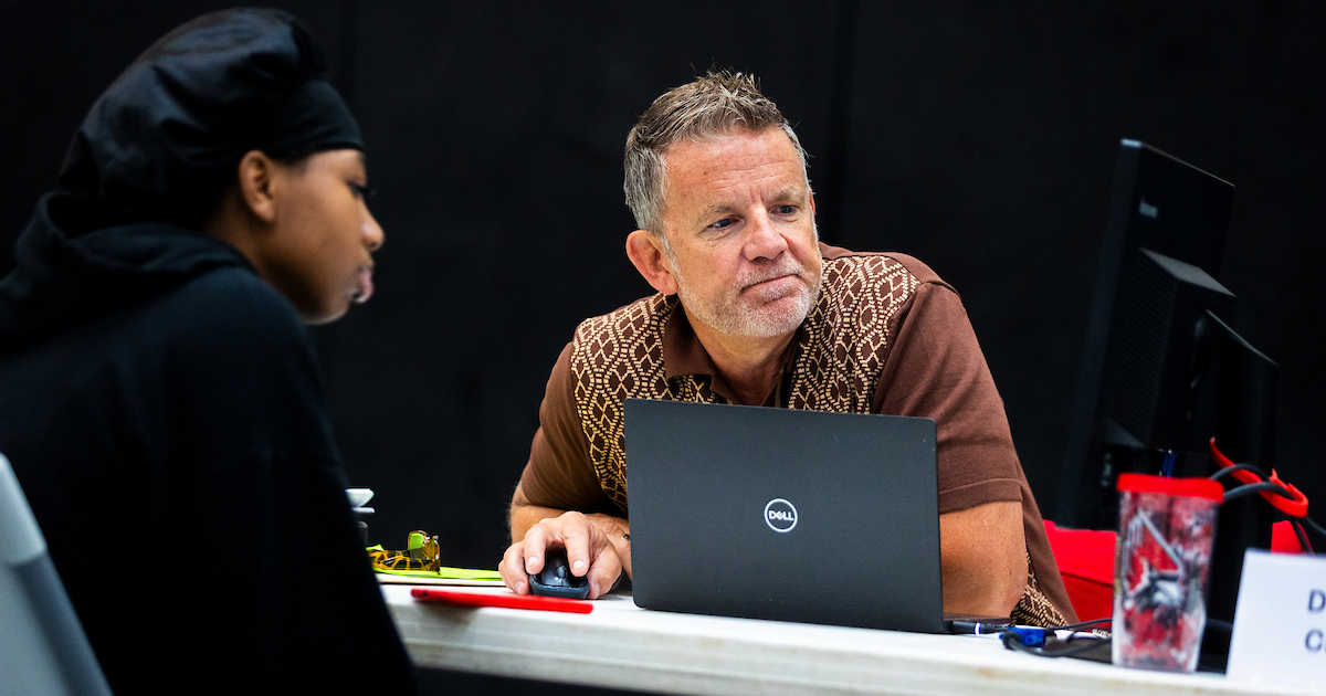 A man and young woman sit across from each other at a table while looking at a computer screen together