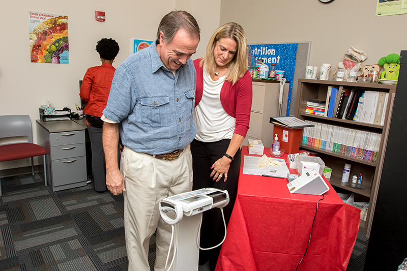 Working Well staff weighing a Ball State employee on a scale