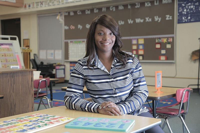 Teachers College student standing at a desk in a classroom. 