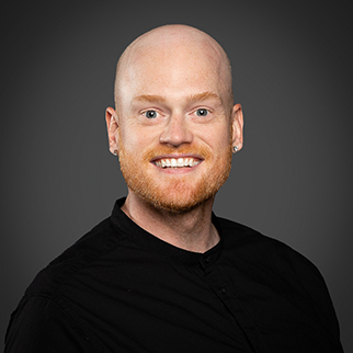 A man wearing a black sweater in front of a grey background
