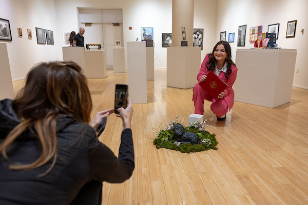 Art student posing with their award winning artwork and their award in the Ned and Gloria Griner Art Gallery.