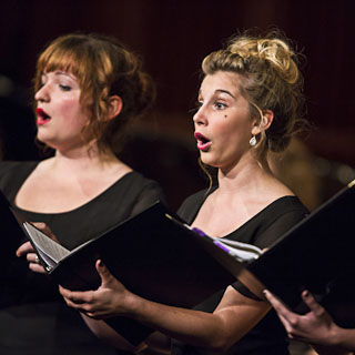 Two female vocalists, one blond and one redhead, singing during a choir concert