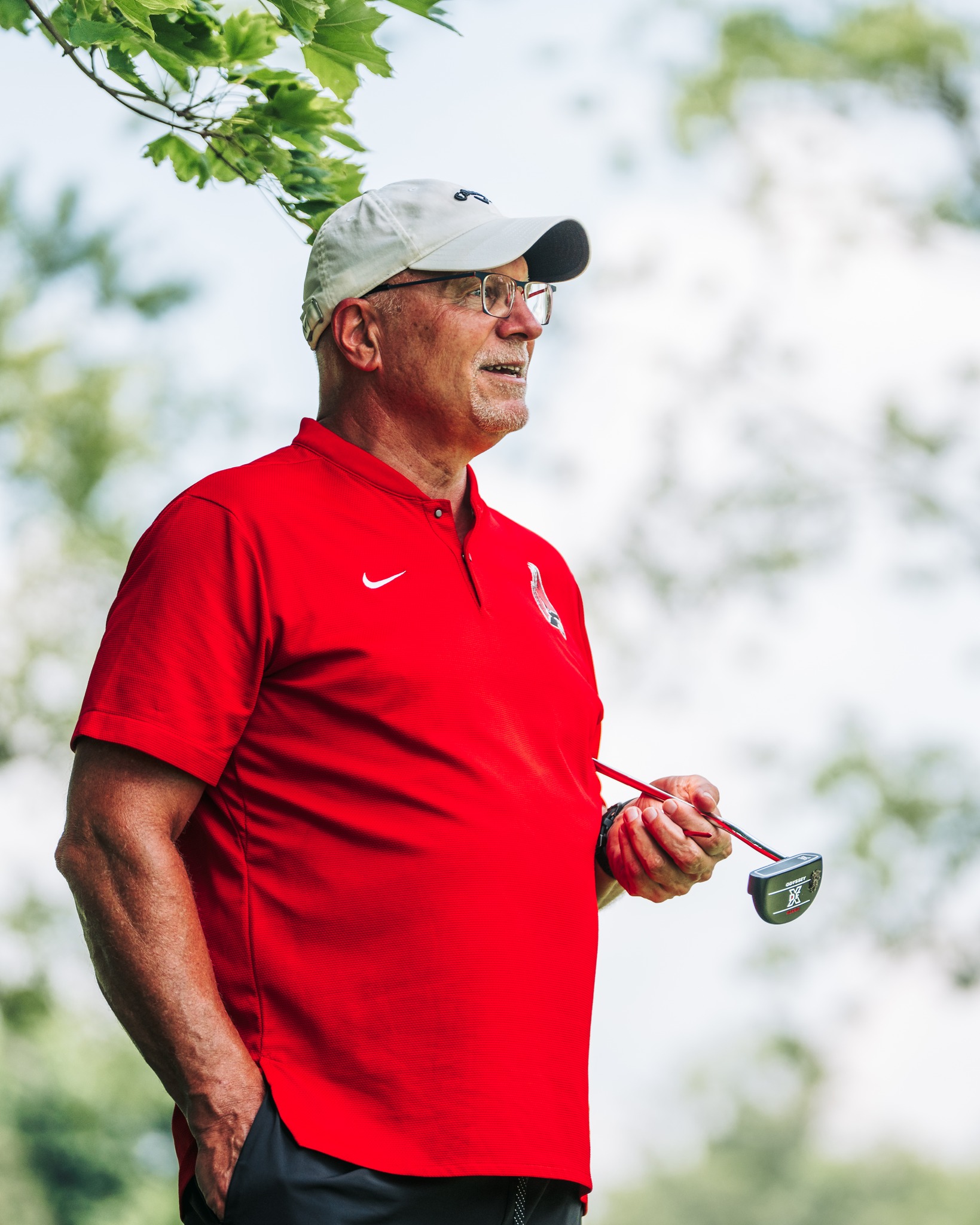 Male in red shirt white hat holding golf club