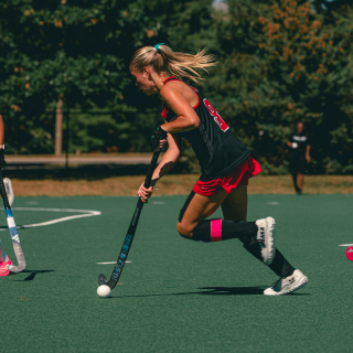 Field Hockey Player with black uniform hitting ball on field