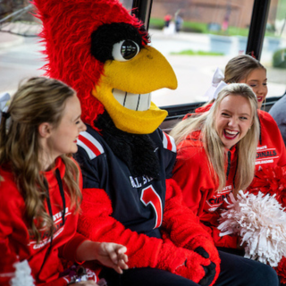 Charlie Cardinal sitting on the Ball State bus with cheerleaders