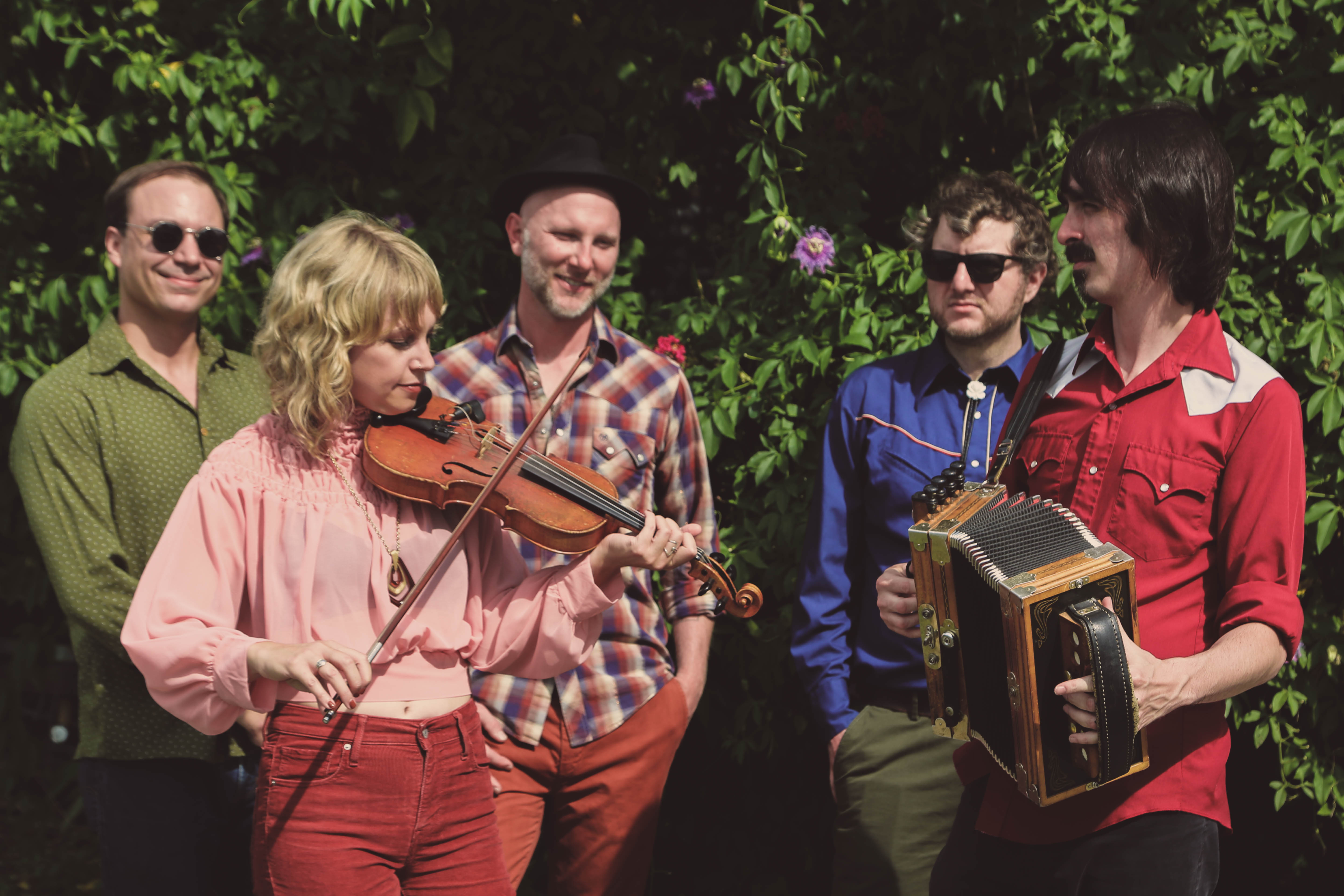 Feufollet pose with their instruments in front of green foliage