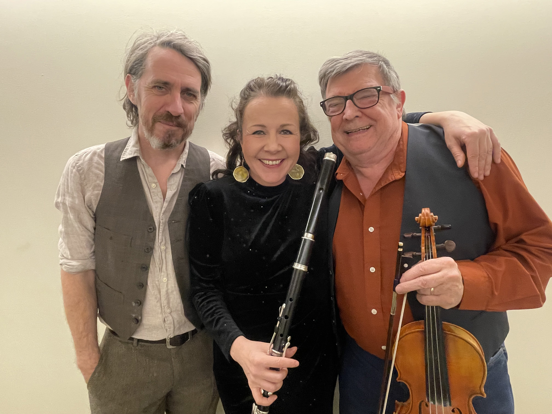 Musicians Kevin Burke, Nuala Kennedy, and Eamon O'Leary pose for a photo together holding their instruments