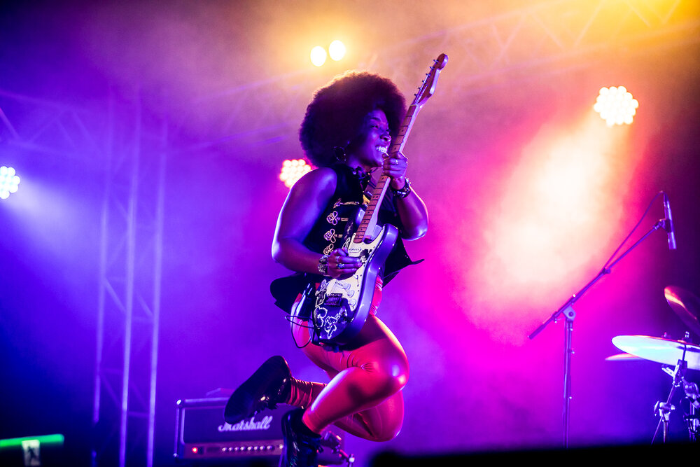 Melody Angel, a Black woman with an afro, performs with her guitar onstage