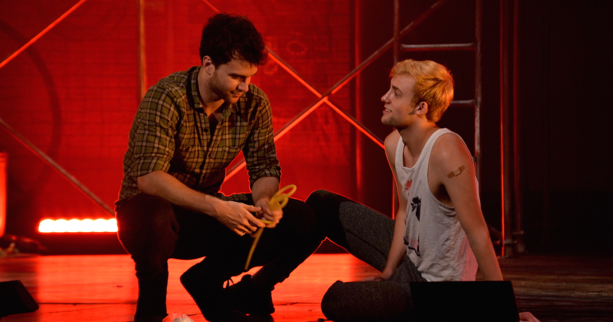 Students sit on stage together during production rehearsal