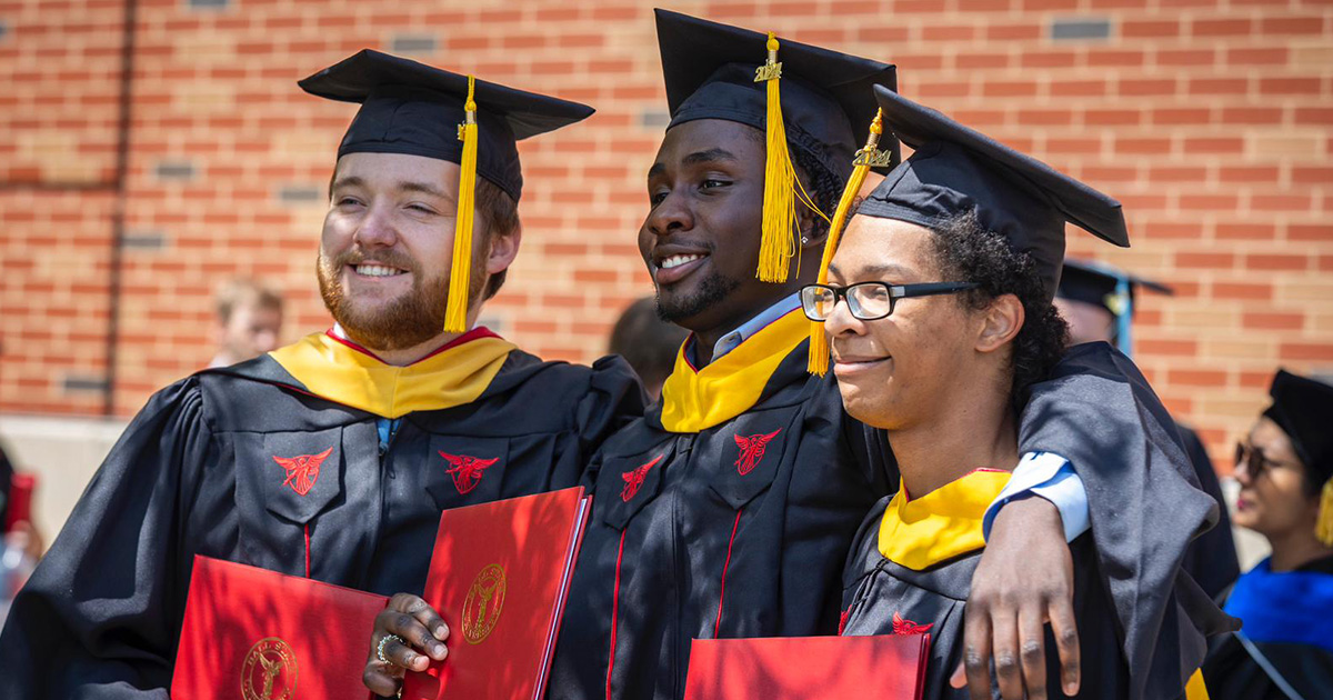 Three graduates take a group photo, each holding their diplomas