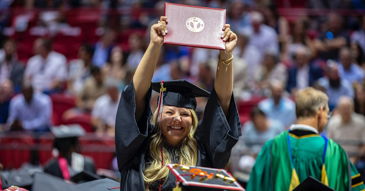 Smiling graduate holding their diploma above their head