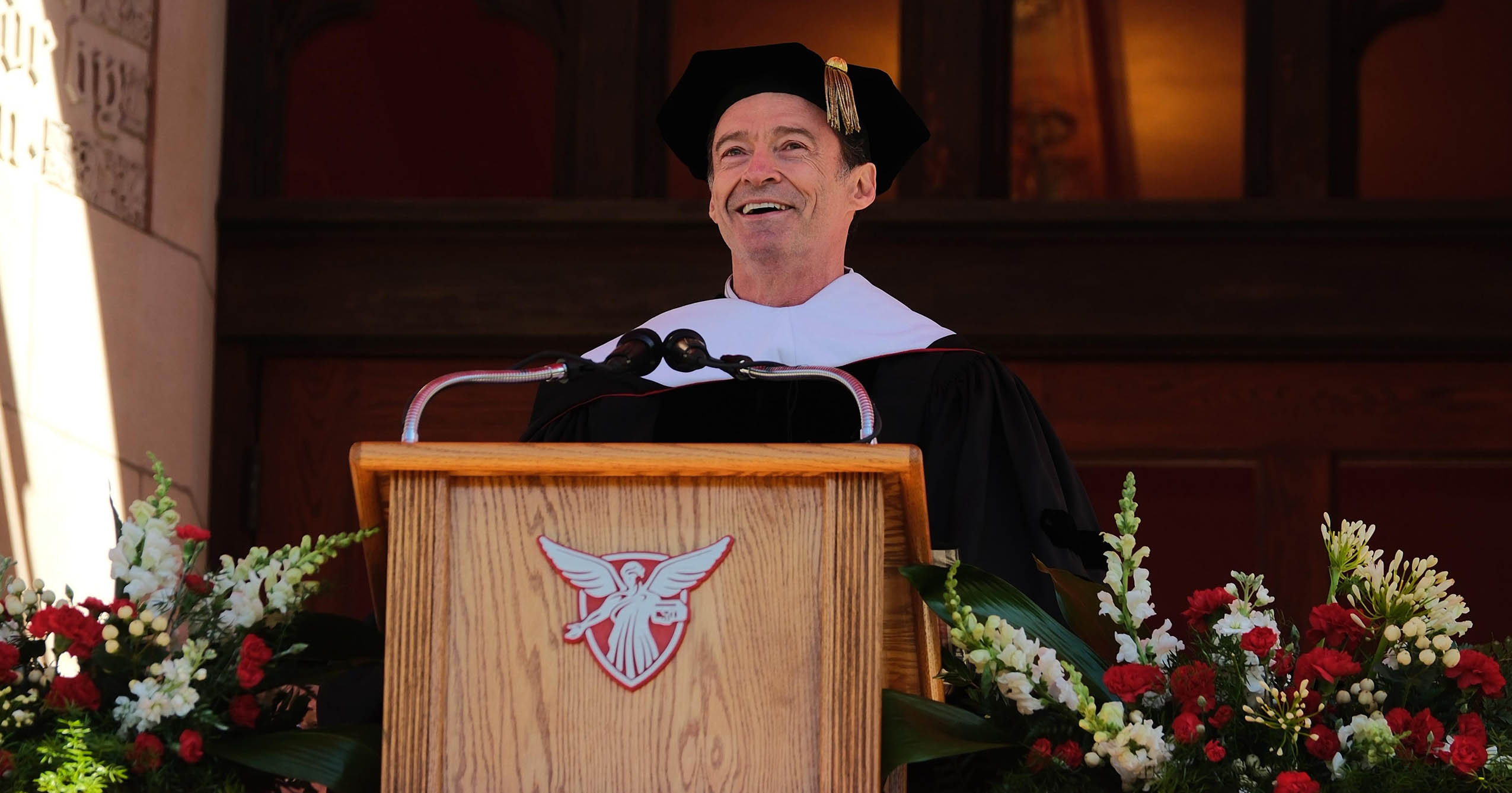 Hugh Jackman smiles while speaking at a Ball State University podium during Spring Commencement.