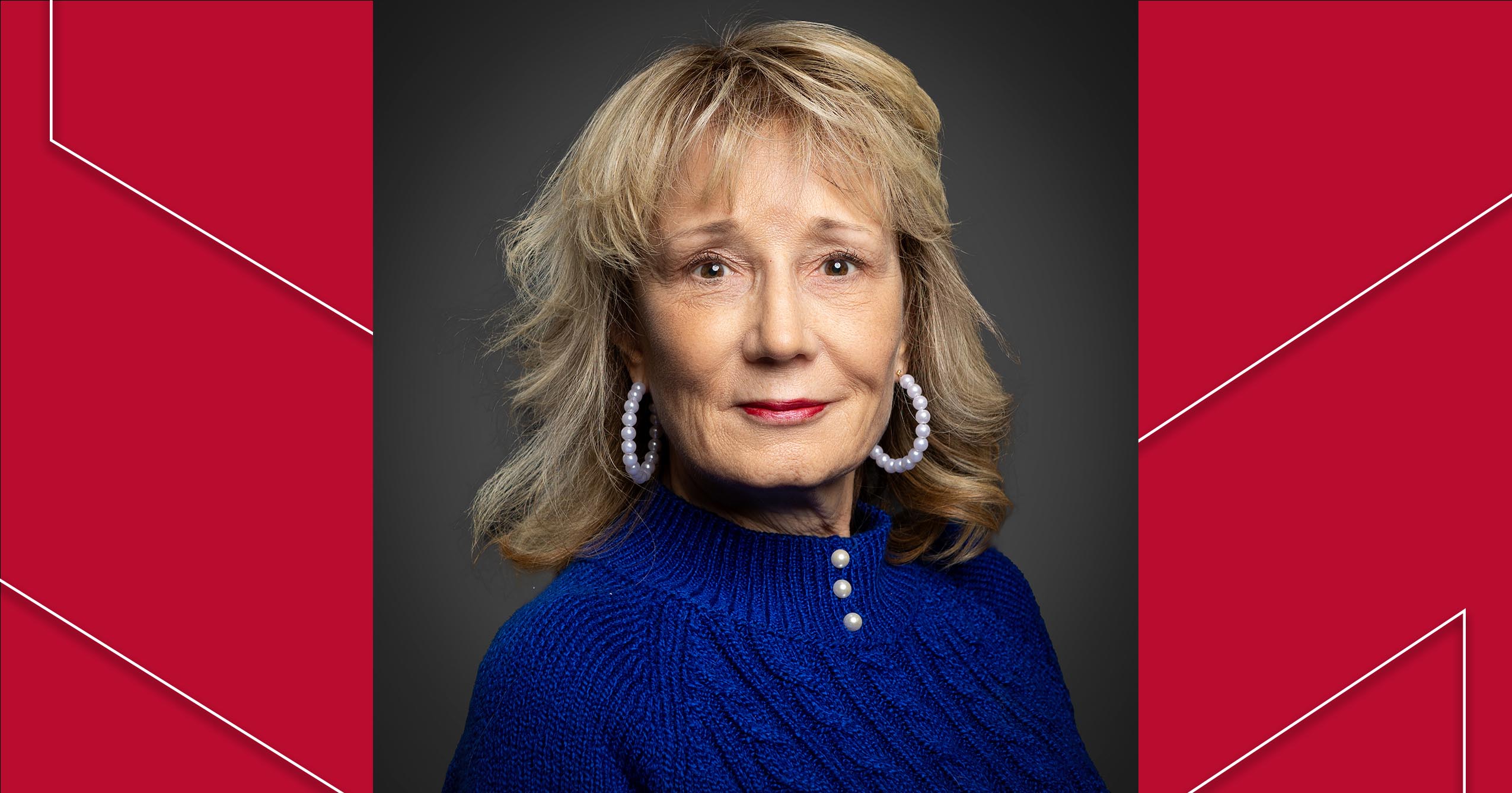 Dr. Renee Twibell poses for a studio portrait wearing a blue sweater and white hoop earrings against a dark background.