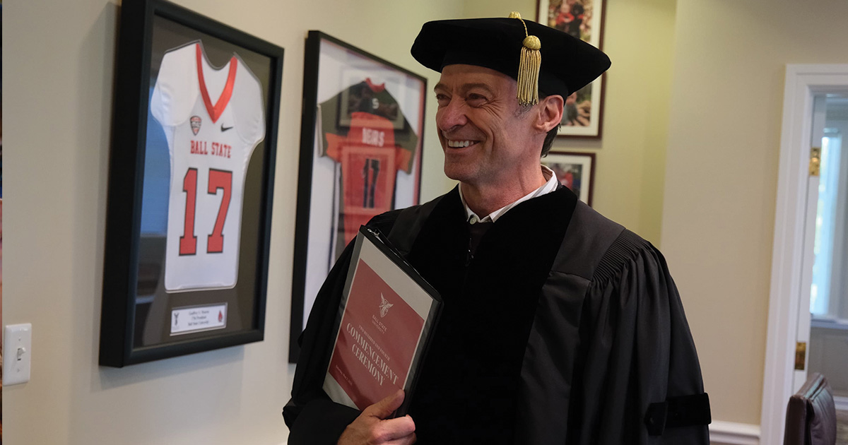 Actor Hugh Jackman poses inside holding binder with Commencement Ceremony on cover