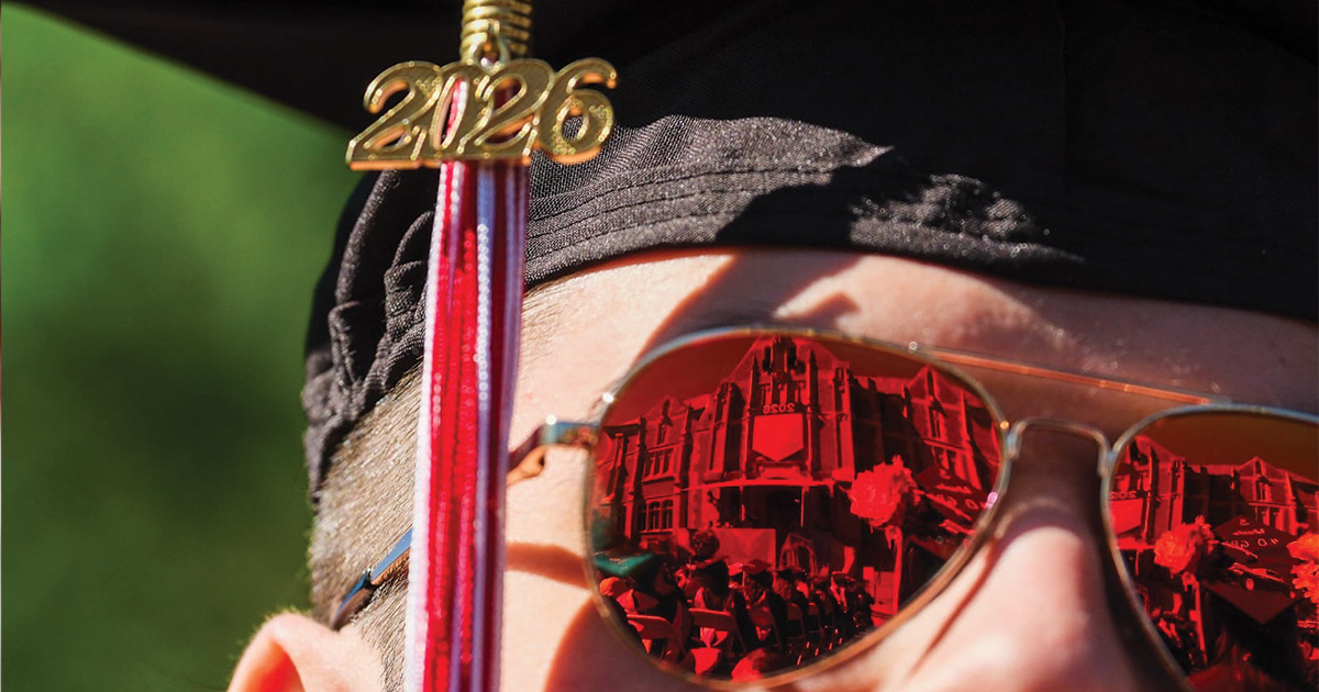 close up of student wearing red mirrored sunclasses with reflection of commencement stage
