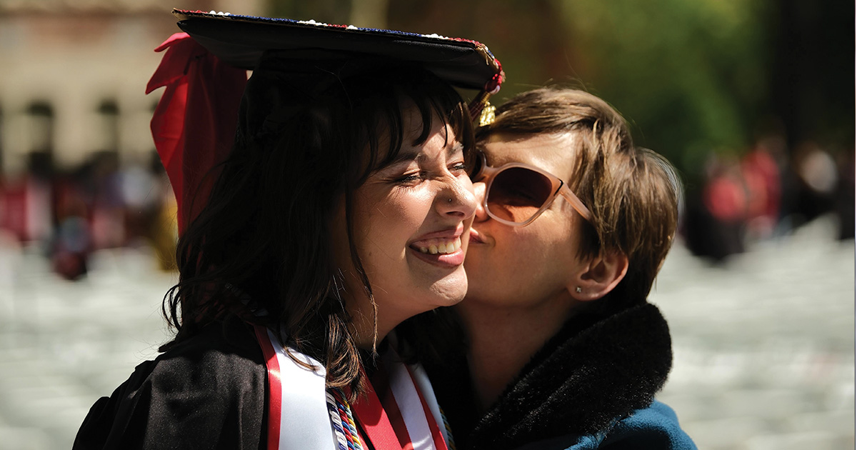 Graduate smiles as mother kisser her cheek