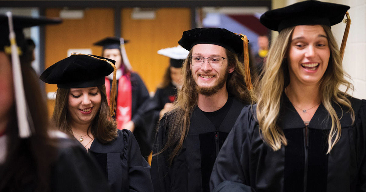 Three graduates smile as they walk together before the commencement ceremony.
